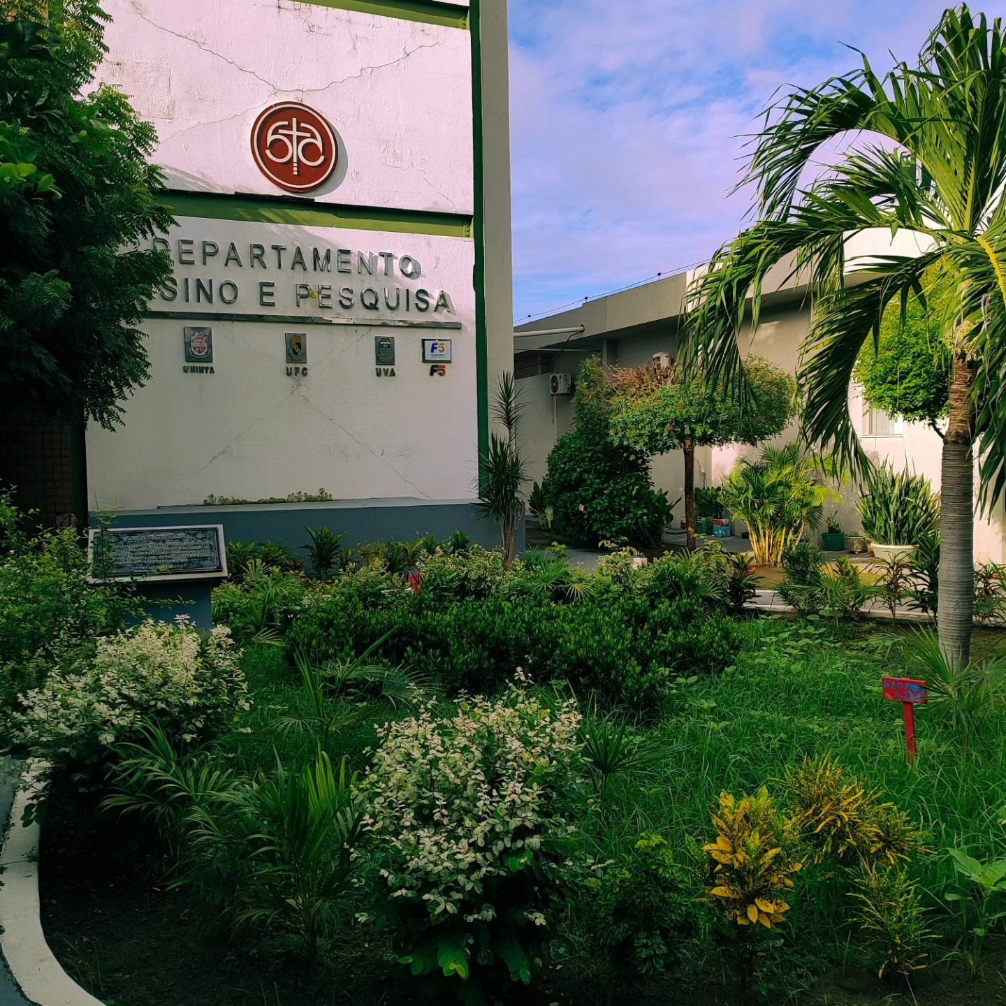 Fachada do Departamento de Ensino e Pesquisa, com jardim e palmeira.