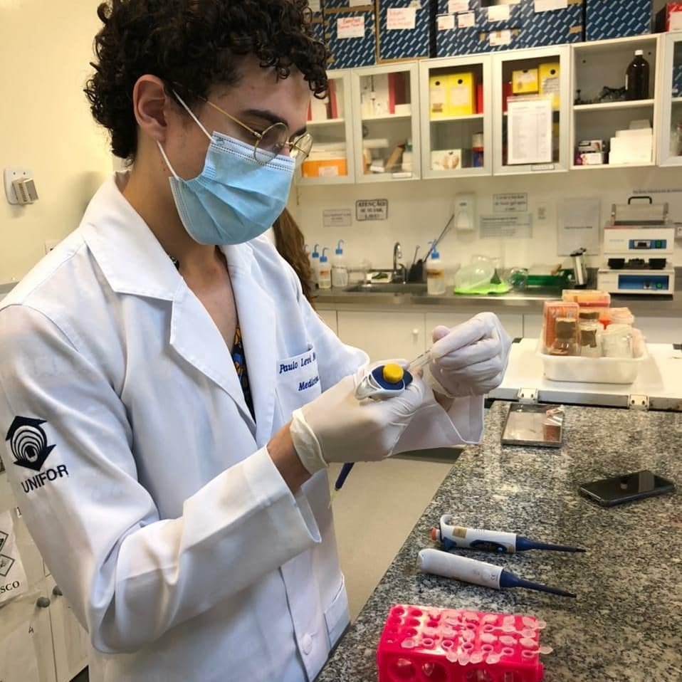 Dr. Paulo Levi de jaleco, luvas e máscara, segurando um tubo no laboratório.